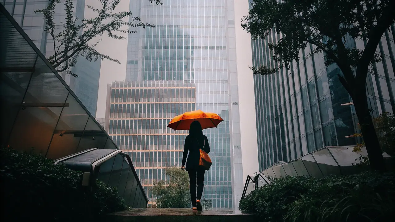 A person with an orange umbrella walking between glass towers and trees
